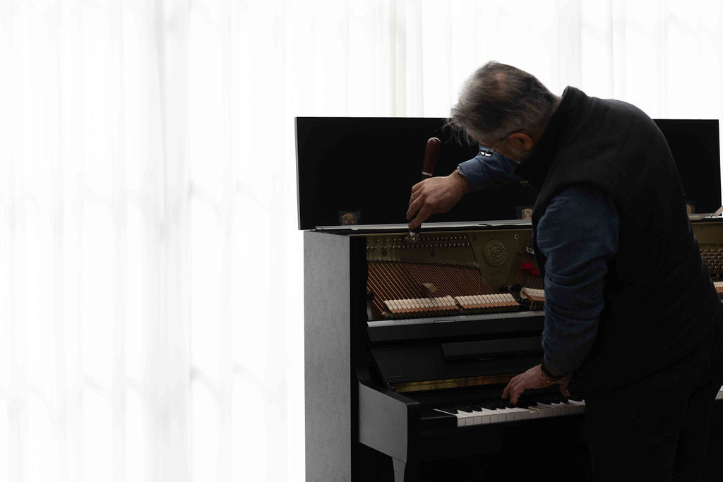 Person tuning a piano with a white curtain in the background
